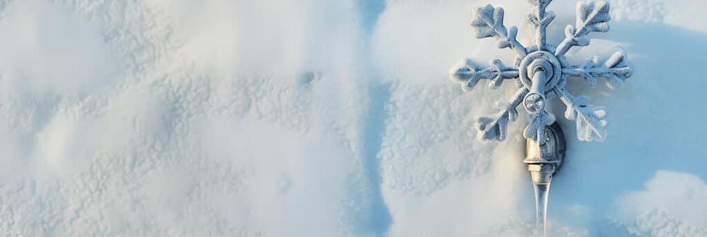 Verschneites Metallwasserhahn im Freien, bedeckt mit Raureif, aus dem klare Eiszapfen hängen, vor einem Hintergrund aus frischem, unberührtem Schnee.